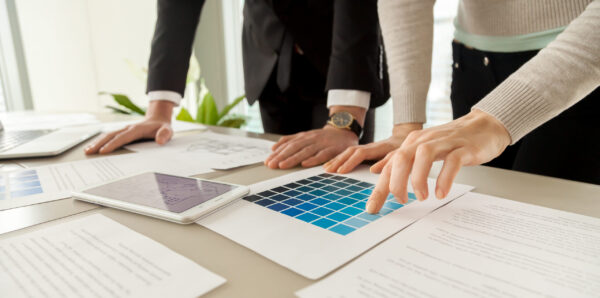 Smiling woman pointing on blue color on pantone swatch on desk while picking house exterior color scheme with architect. Female planning apartments decoration with interior designer. Close up view